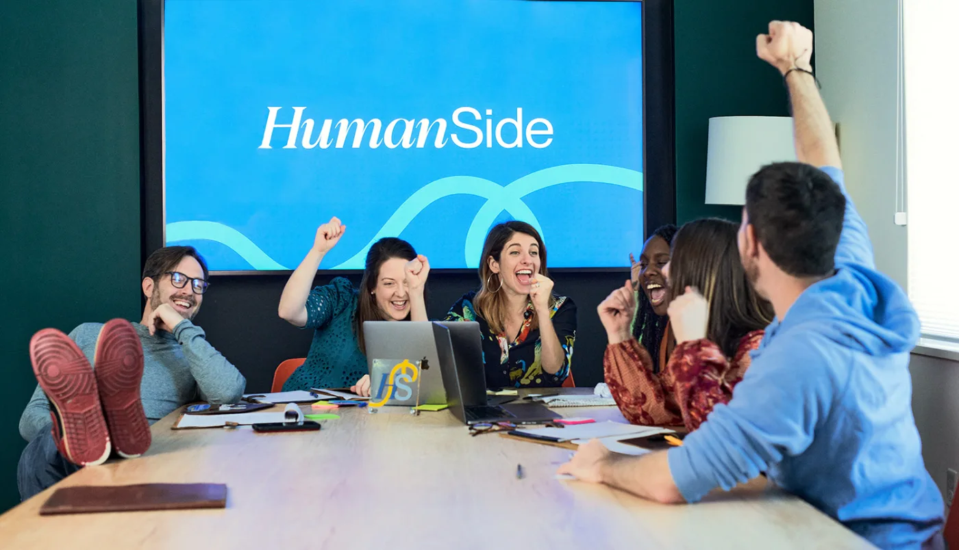 The HumanSide team celebrating in front of the HumanSide brand wall.